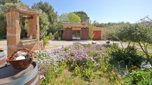 Un espacio al aire libre rústico con un arco de piedra, construcciones de madera y diversas plantas en flor.