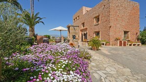 Un edificio de piedra con un patio, palmeras y diversas flores.