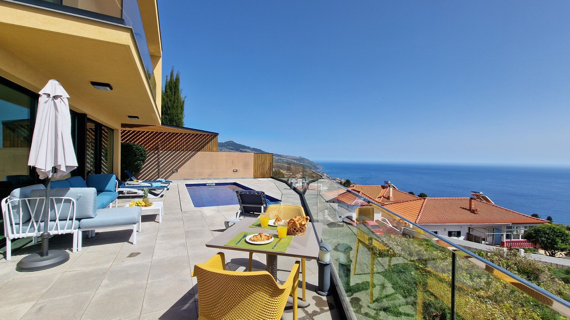 A balcony with a pool, outdoor seating, and a view of the sea.