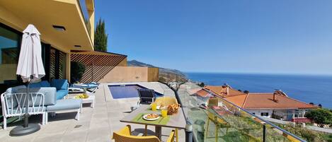 A balcony with a pool, outdoor seating, and a view of the sea.
