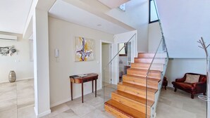 A modern interior with a wooden staircase, a glass railing, a red leather sofa, and a minimalist decor. - Eden Sun - Luxury Villa w/ocean View by LovelyStay (Prazeres)