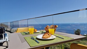 A table with croissants, a glass of orange juice, and a basket of croissants on a balcony overlooking a scenic view. - Eden Sun - Luxury Villa w/ocean View by LovelyStay (Prazeres)