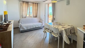 A room with a bed, a dining table with chairs, a small kitchen area, and an air conditioning unit. - New valmar Two-room apartment 56 - Via del Lentischio (Costa Rei)