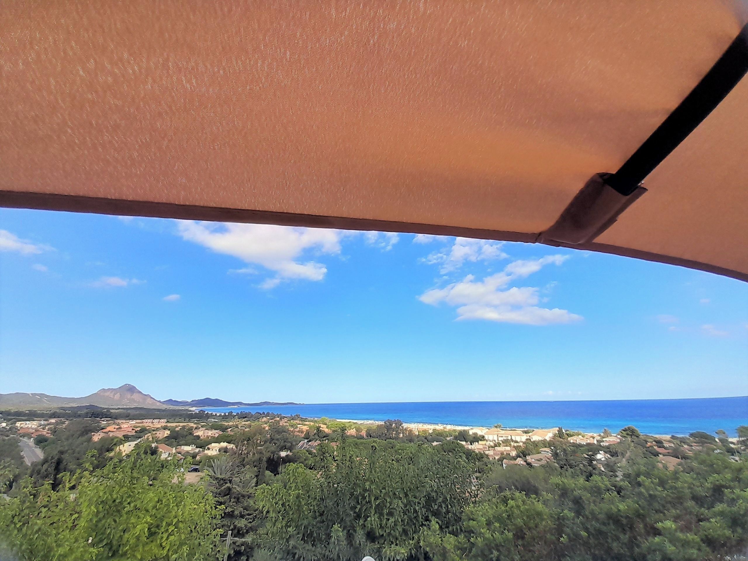 A view from inside a vehicle, looking out at a coastal landscape with a mountain in the distance, under a clear sky.