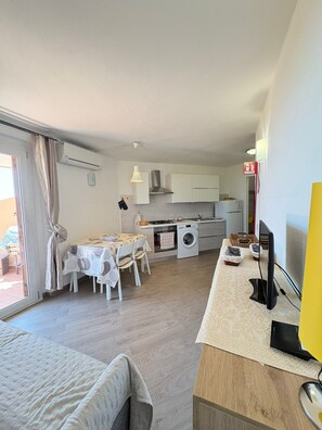 Un espace de vie compact comprenant un coin cuisine, un coin repas et un lit.