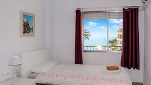 A hotel room with a bed, a nightstand, a lamp, a window with curtains, and a painting on the wall. - Acapulco Playa 308 by Casasol (Nerja)