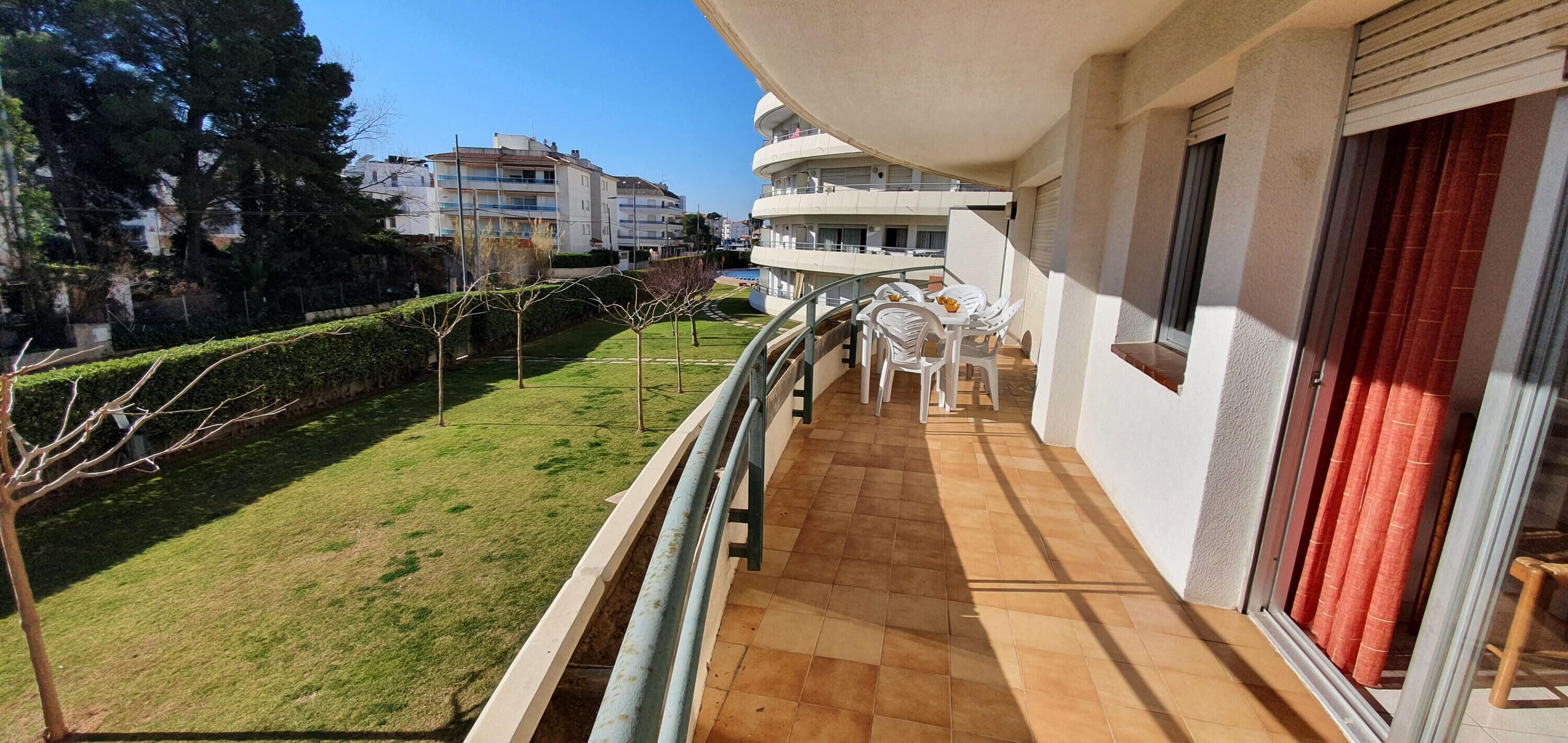 Un balcone con pavimento piastrellato, sedie di plastica bianca e un tavolo con una ciotola di frutta.