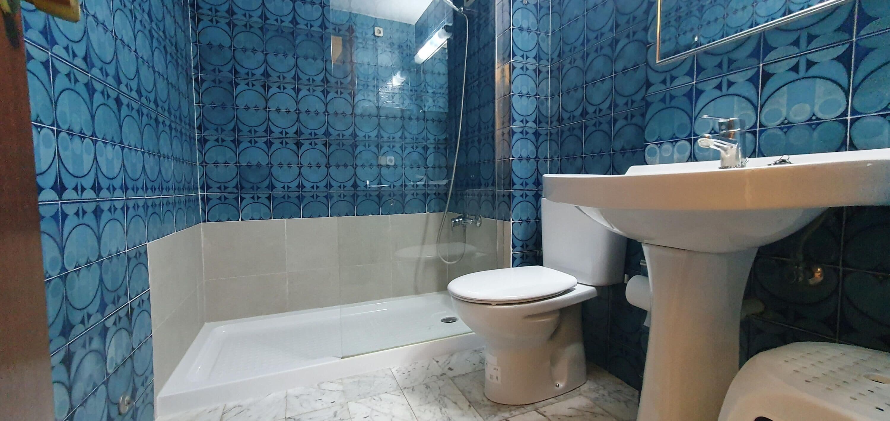 A bathroom with blue patterned tiles, a white toilet, a bathtub, and a sink.