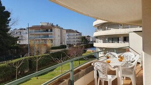 Un balcon avec une table et des chaises, donnant sur un jardin et des immeubles.