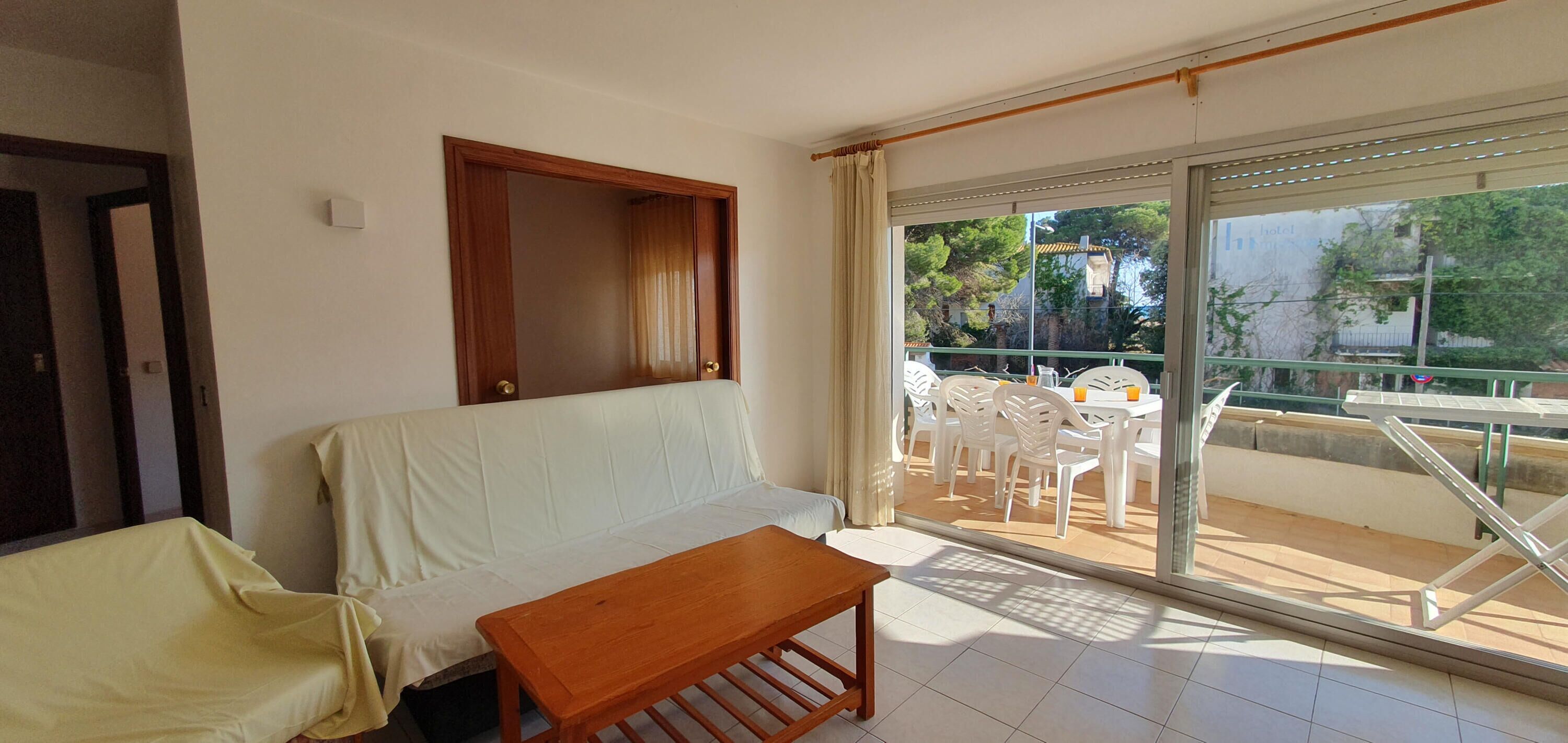 Une pièce comprenant un canapé, une table en bois et un balcon avec des chaises et une table en plastique.