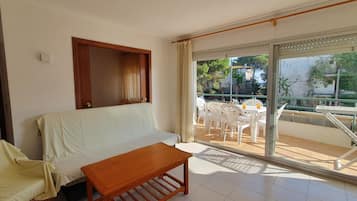 Une pièce comprenant un canapé, une table en bois et un balcon avec des chaises et une table en plastique.