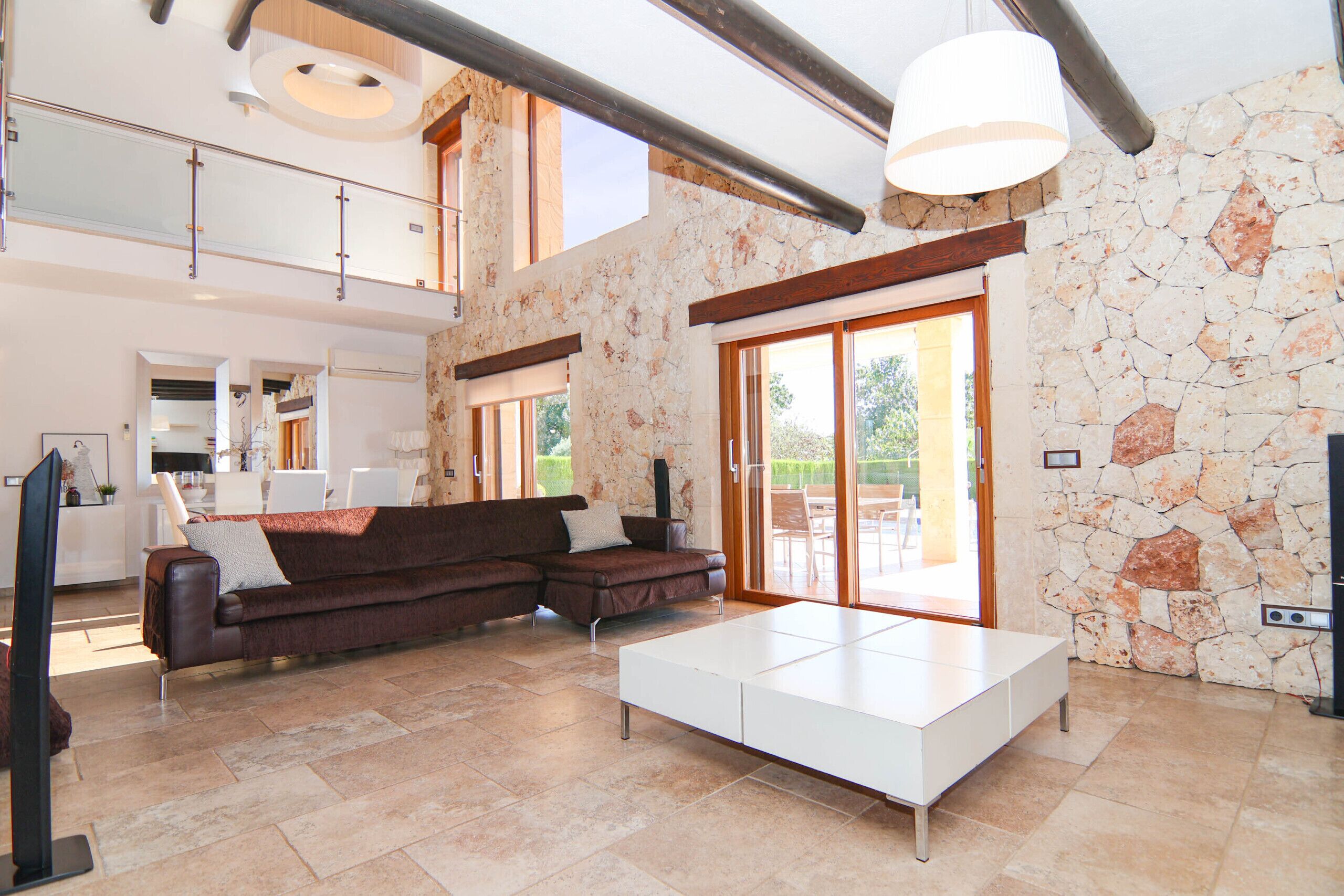 A spacious living area with a brown sectional sofa, a white coffee table, and a stone wall.