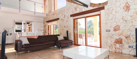 A spacious living area with a brown sectional sofa, a white coffee table, and a stone wall.