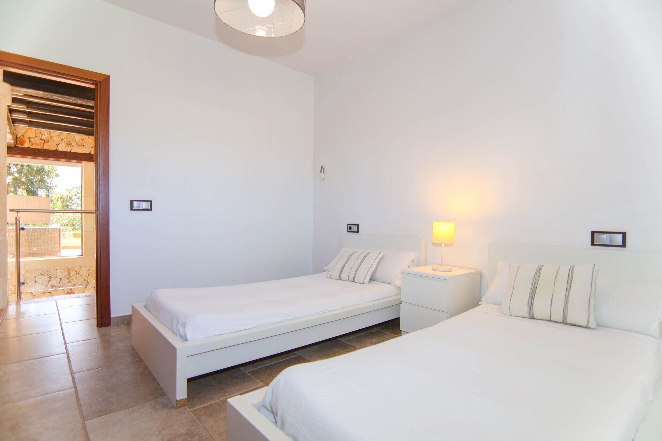 Un dormitorio con dos camas individuales, una mesita de noche, una lámpara y una puerta que da a un espacio al aire libre.