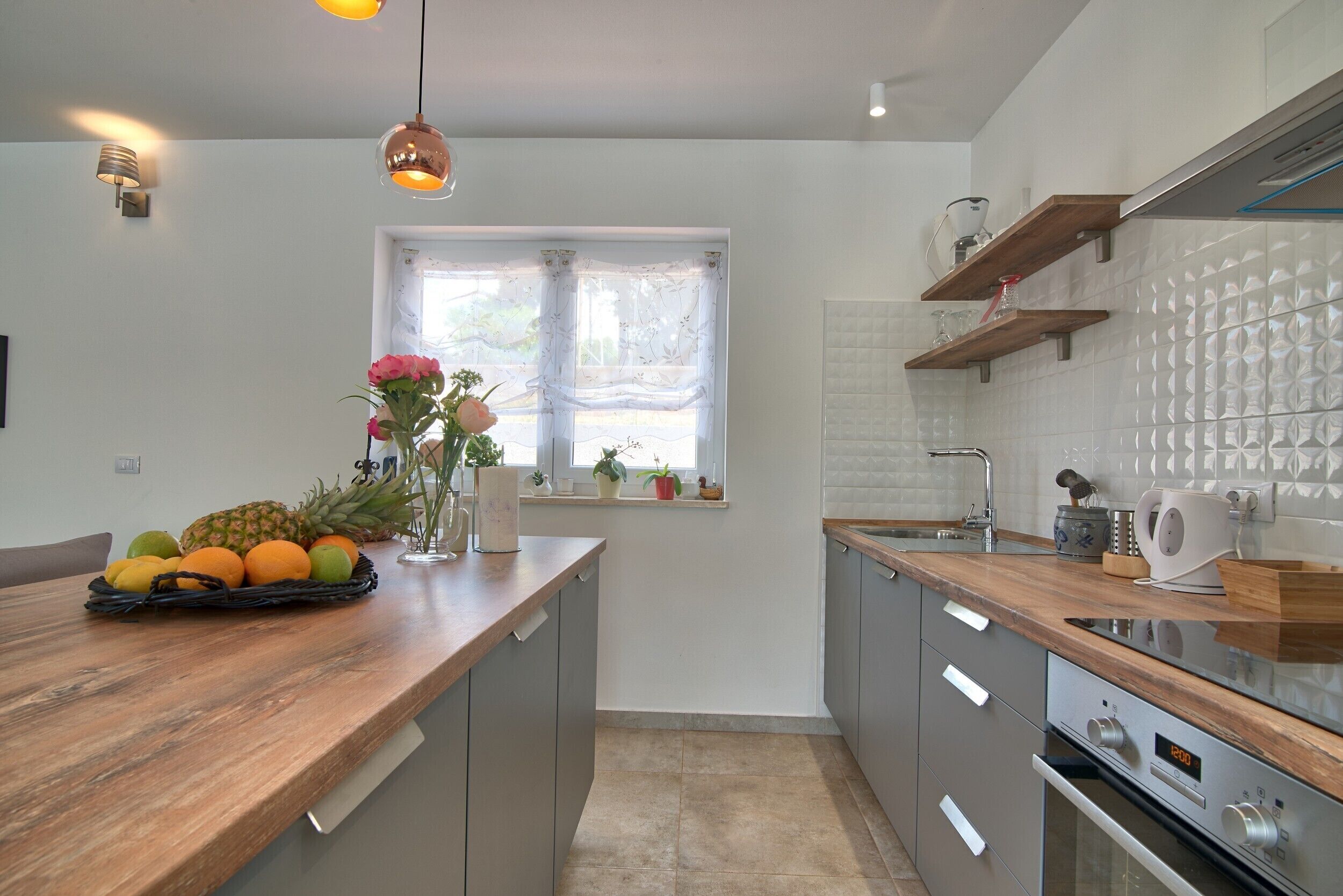 Une cuisine moderne avec des plans de travail en bois, un four encastré et une fenêtre ornée de rideaux légers.