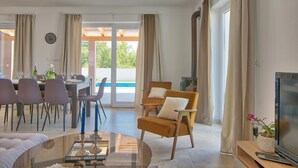 Ein modernes Wohnzimmer mit Essbereich, Fernseher und Blick ins Freie.