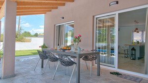 Eine Terrassengruppe mit Tisch und Stühlen, eine Glastür, die in eine Küche f ührt, und Blick ins Freie.