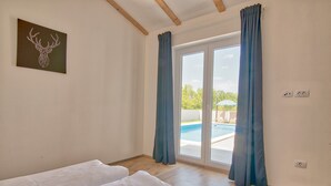 Ein Zimmer mit einem Bett, einem Hirschbild und Blick auf einen Swimmingpool durch eine Glastür.