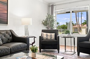 A living room with a leather sofa, a black armchair with a striped pillow, a floor lamp, and a small table with a plant.
