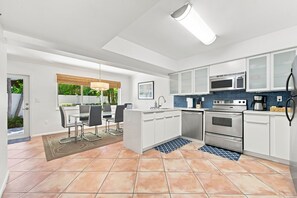 A modern kitchen with white cabinets, stainless steel appliances, and a dining area with a table and chairs.