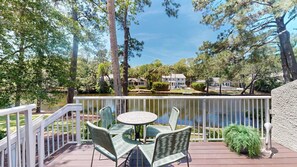 A deck with chairs and a table overlooking a lake, surrounded by trees and houses. - Recently Renovated Lagoon View Townhouse! (Hilton Head)