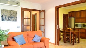 Ein Wohnzimmer mit orangefarbenem Sofa, einem Esstisch mit Stühlen und einer Küchenzeile mit Holzausbau und Geräten.