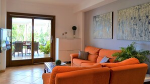 Ein Wohnzimmer mit einem orangefarbenen Sofa, einem Fernseher und einer Schiebetür, die auf eine Außenpatio führt.
