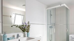 A modern bathroom with a white sink, wooden vanity, a glass shower enclosure, and patterned floor tiles.