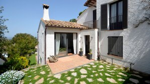 Une maison blanche avec un toit en tuiles, un balcon et un jardin avec une pelouse et des fleurs aux motifs variés.