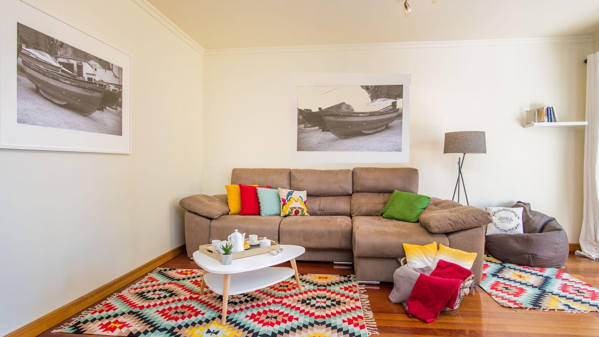 A living room with a brown sofa, colorful cushions, a white coffee table, a patterned rug, and two wall-mounted lamps.