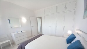 Een slaapkamer met een bed, een dressoir, een spiegel en een kledingkast.