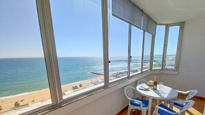 Een balkon met uitzicht op het strand en de oceaan. Er staat een tafel met stoelen en een fles wijn.