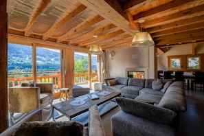 Un salon chaleureux avec un grand canapé d’angle, un plafond en bois et une vue sur les montagnes.