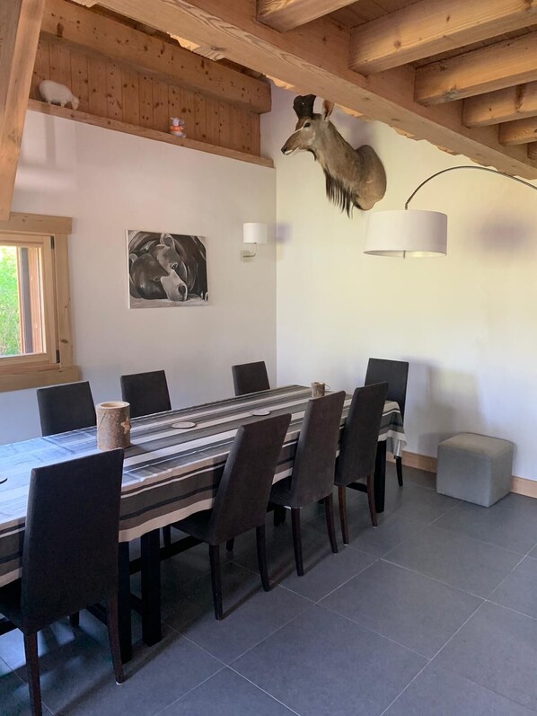 A dining area with a long table, chairs, a mounted deer head, a wall-mounted lamp, and a painting. - Spacious and design chalet (Samoëns)