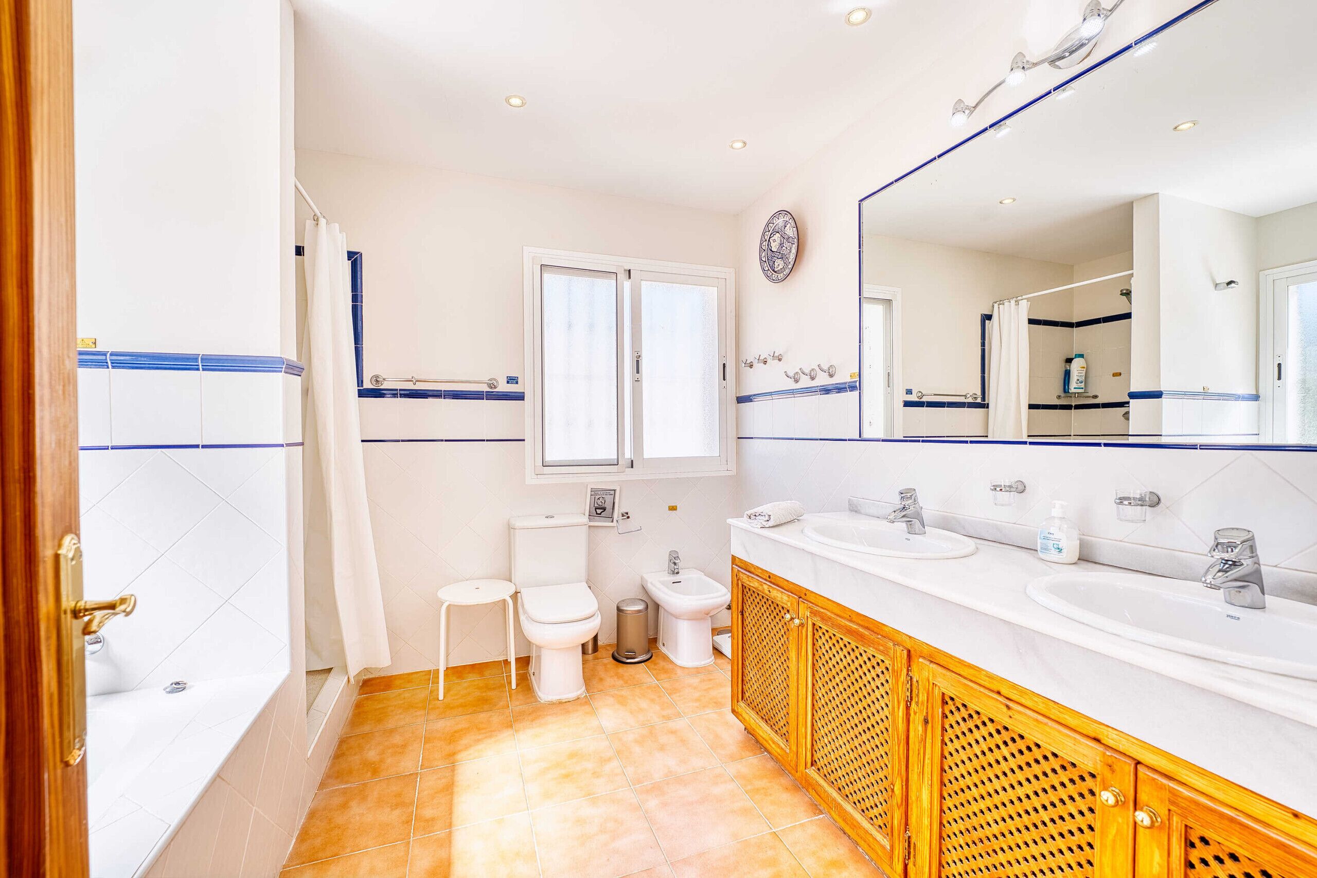 A bathroom with a bathtub, two toilets, a bidet, and a large mirror.