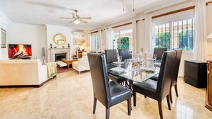 A spacious living room with a fireplace, a dining area with a glass table and chairs, and a television.