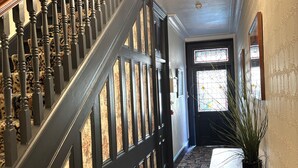 Un magnifique escalier en bois foncé, surmonté d’un lustre, mène à une pièce dont le sol est recouvert d’un tapis à motifs et qui est agrémentée d’une plante en pot.