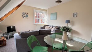 Un salon confortable avec un canapé, des fauteuils verts, une table en verre et un téléviseur.