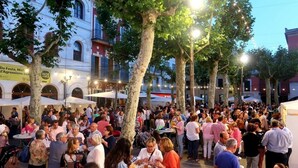Un área de comedor al aire libre concurrida, con mesas y sillas, rodeada de árboles y edificios.