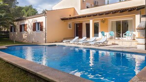 Una villa moderna con piscina, tumbonas y un porche cubierto.