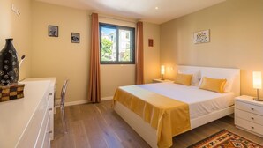 Ein Schlafzimmer mit Bett, Nachttischen, Fenster mit Vorhängen, Schreibtisch mit Stuhl und einer dekorativen Vase.