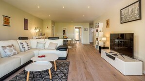Ein modernes Wohnzimmer mit Sofa, Couchtisch und Fernseher. Ein Flur führt zu einem Essbereich.