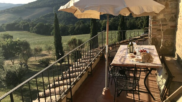Een balkon met een tafel en stoelen, een witte parasol en uitzicht op een glooiend landschap.