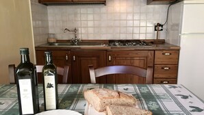Een keuken met houten kastjes, een spoelbak en een fornuis. Op een tafel staan twee flessen olijfolie en een bord met brood.