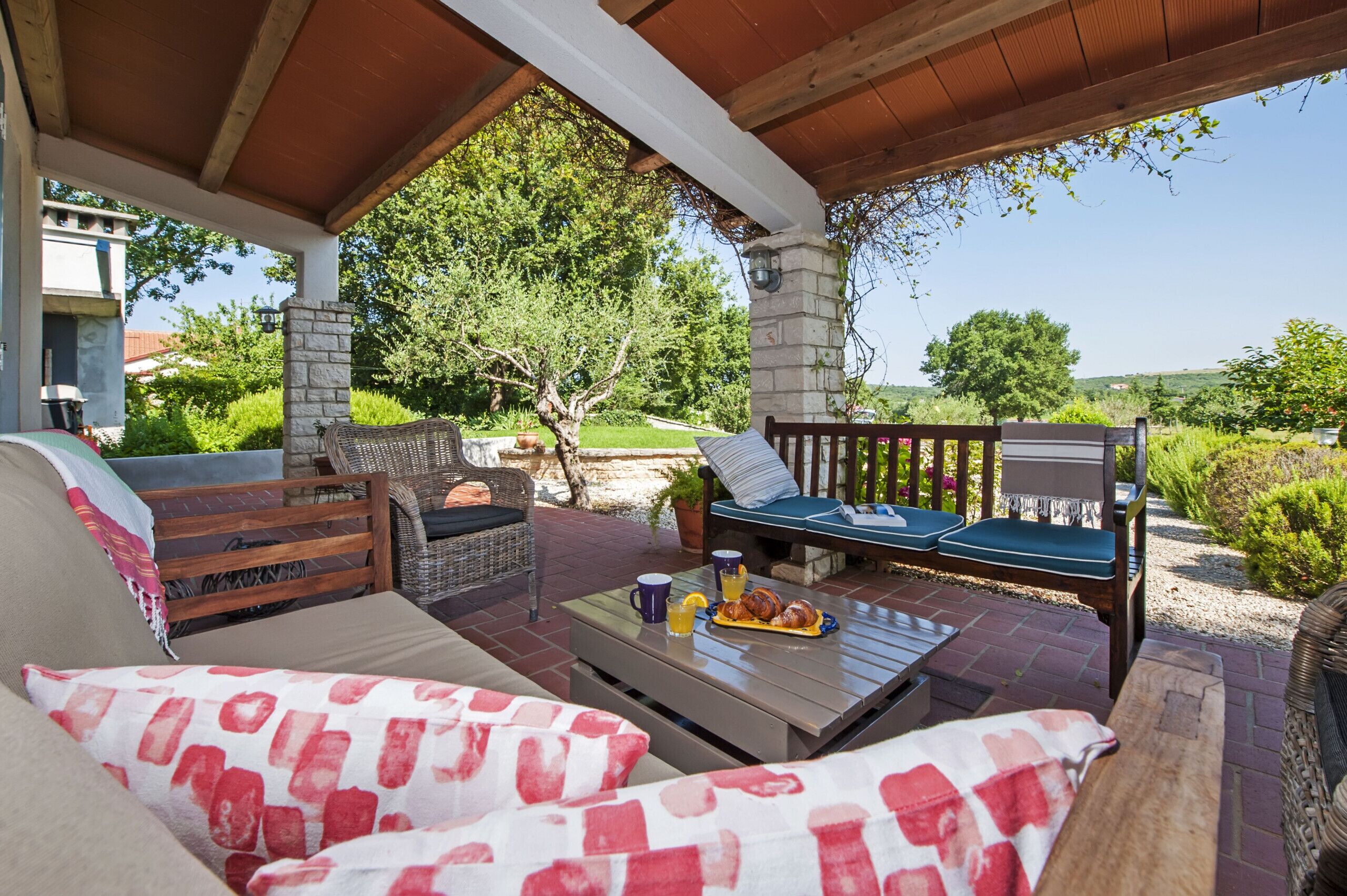 An outdoor patio with wicker furniture, a stone pillar, and a view of the surrounding greenery.