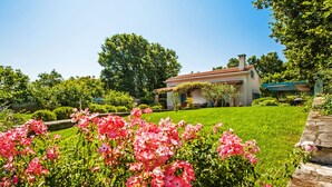 Ein Haus mit rotem Ziegeldach, umgeben von einem gepflegten Garten mit rosa Blumen und grünem Rasen.