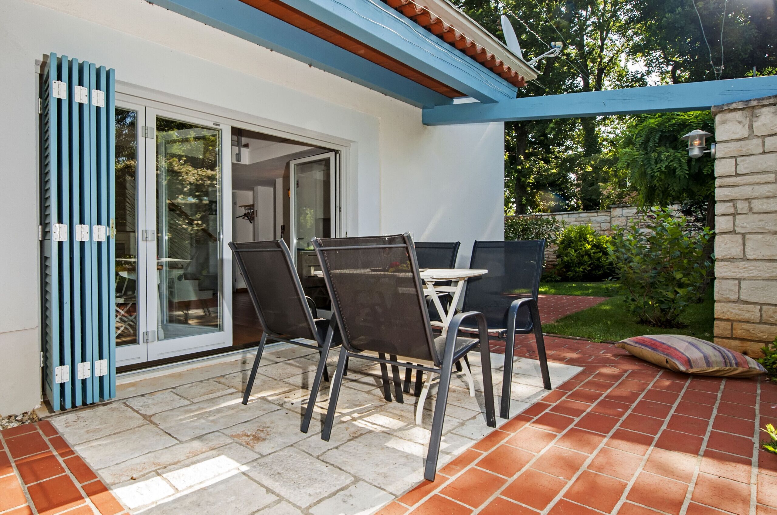 Une terrasse extérieure avec une table et des chaises, un mur en pierre et une porte vitrée donnant sur un espace abrité.