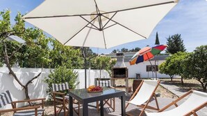 Een terras buiten met een tafel, stoelen en een barbecue.