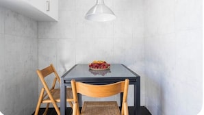 Een moderne keuken met een glazen tafel, twee houten stoelen, een fruitschaal en een hanglamp.