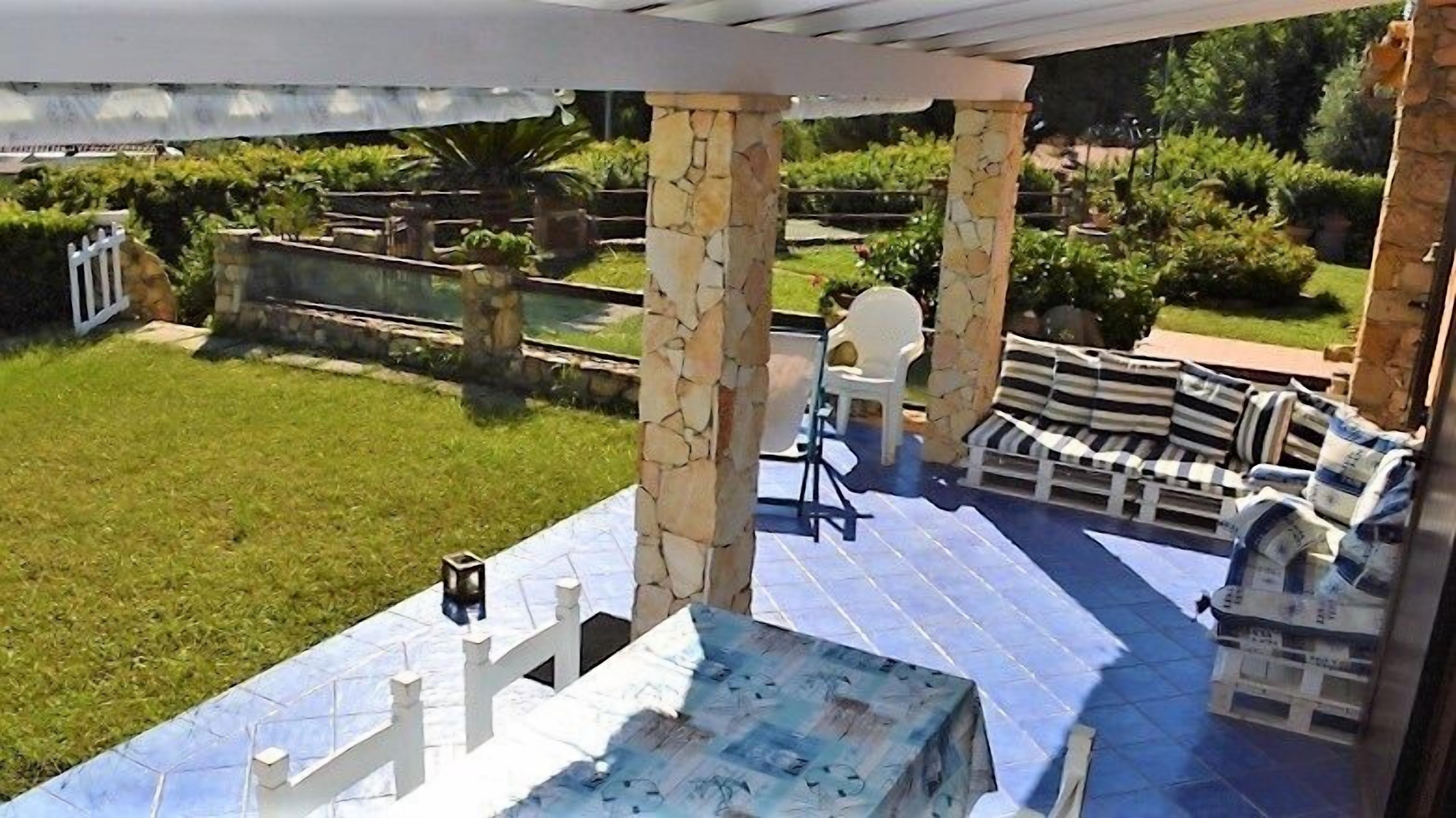 A covered patio with a table and chairs, stone pillars, and a view of a well-maintained garden.